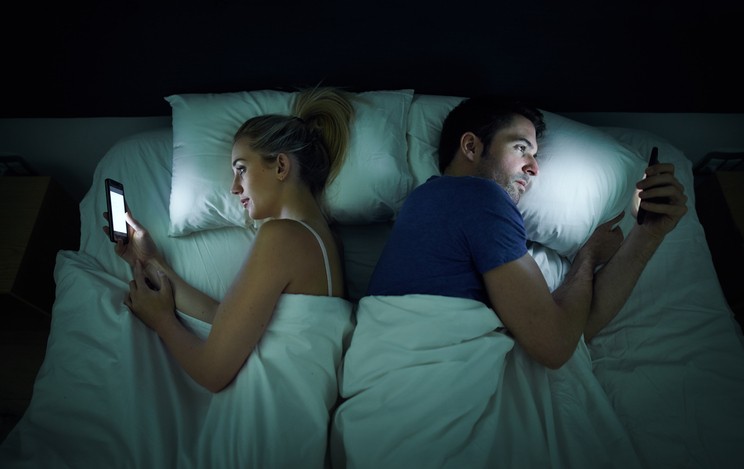Małżeństwo przeglądające telefon leżąc w łóżku